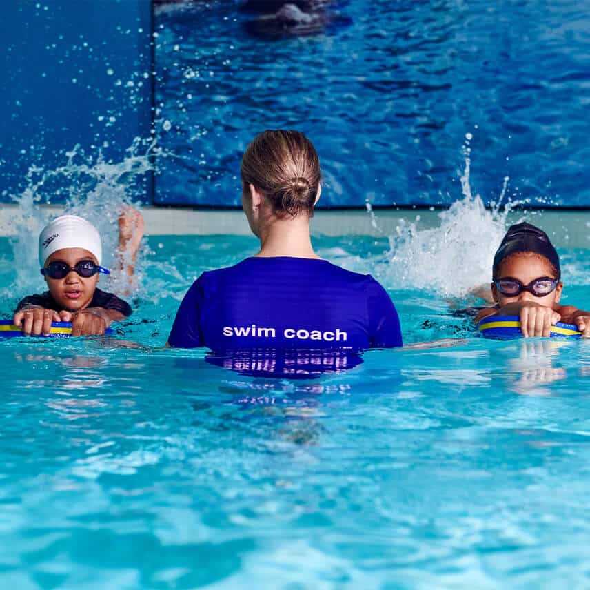 A swim coach teaches two children how to swim during a swimming lesson in a Virgin Active gym's pool.